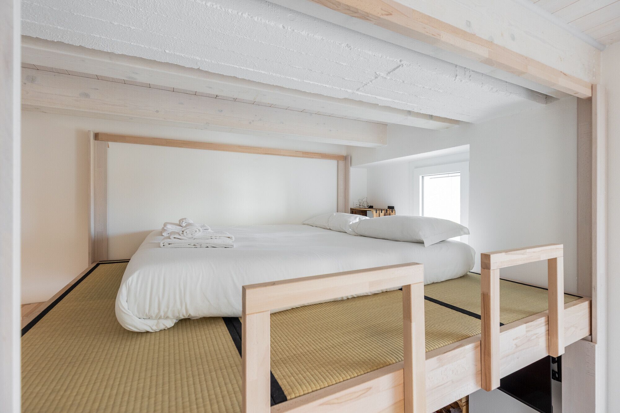 A minimalist room with a bed, a small bedside table, and a window.