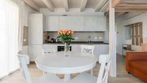 Una cocina moderna con armarios blancos, una mesa redonda de comedor con sillas blancas y un florero con flores.