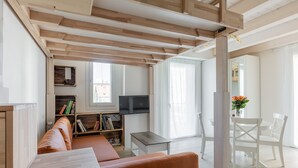 Una sala de estar moderna con vigas de madera a la vista, un sofá, un televisor y una zona de comedor con sillas.
