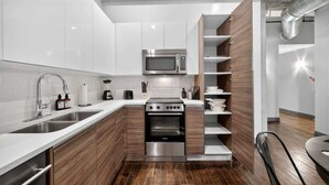 Una cucina moderna con mobili bianchi, un forno a microonde integrato, un forno in acciaio inossidabile ed elementi a mensola in legno.