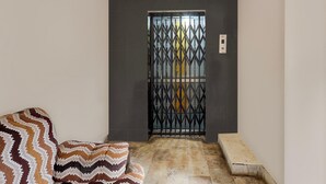 Une pièce avec un canapé à motifs, un banc, un sol carrelé et une porte surmontée d’un portail en métal.