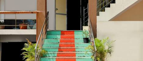 Una escalera con una banda roja, plantas en macetas y una puerta que da a un espacio interior.