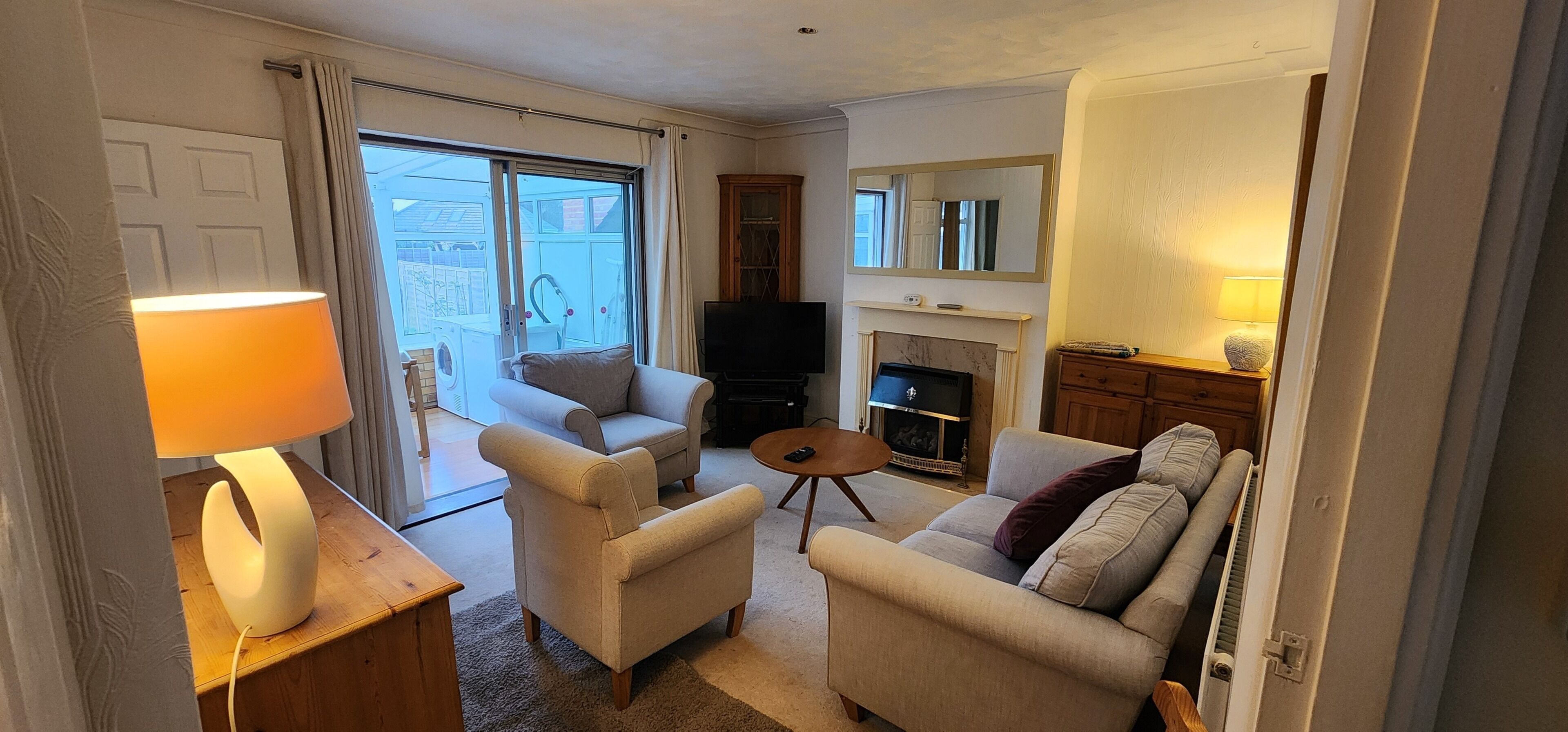A living room with a sofa, armchairs, a TV, a fireplace, and a sliding glass door leading to a balcony.