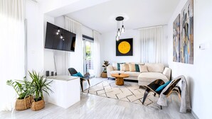 A modern living room with a flat-screen TV, a sofa, a coffee table, and a dining area. - Luxury 5BR Villa in Paphos | Private Pool, Hot Tub & Sea Views | Family Retreat (Kissonerga)