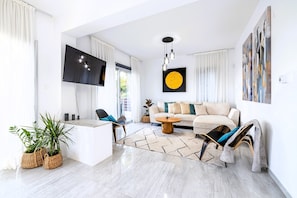 A modern living room with a flat-screen TV, a sofa, a coffee table, and a dining area. - Luxury 5BR Villa in Paphos | Private Pool, Hot Tub & Sea Views | Family Retreat (Kissonerga)