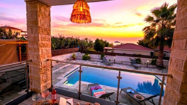 A balcony with a pool, a hanging light fixture, and a view of the sunset. - Luxury 5BR Villa in Paphos | Private Pool, Hot Tub & Sea Views | Family Retreat (Kissonerga)