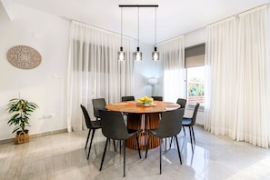 A dining area with a round table, chairs, hanging lights, and a plant. - Luxury 5BR Villa in Paphos | Private Pool, Hot Tub & Sea Views | Family Retreat (Kissonerga)