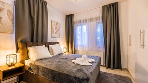 A bedroom with a bed, nightstand, lamp, and a view of the outdoors through sheer curtains. - Luxury 5BR Villa in Paphos | Private Pool, Hot Tub & Sea Views | Family Retreat (Kissonerga)