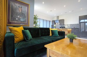 Ein modernes Wohnzimmer mit einem dunkelgrünen Sofa, gelben Kissen, einem Holztisch und einem gerahmten Bild an der Wand.