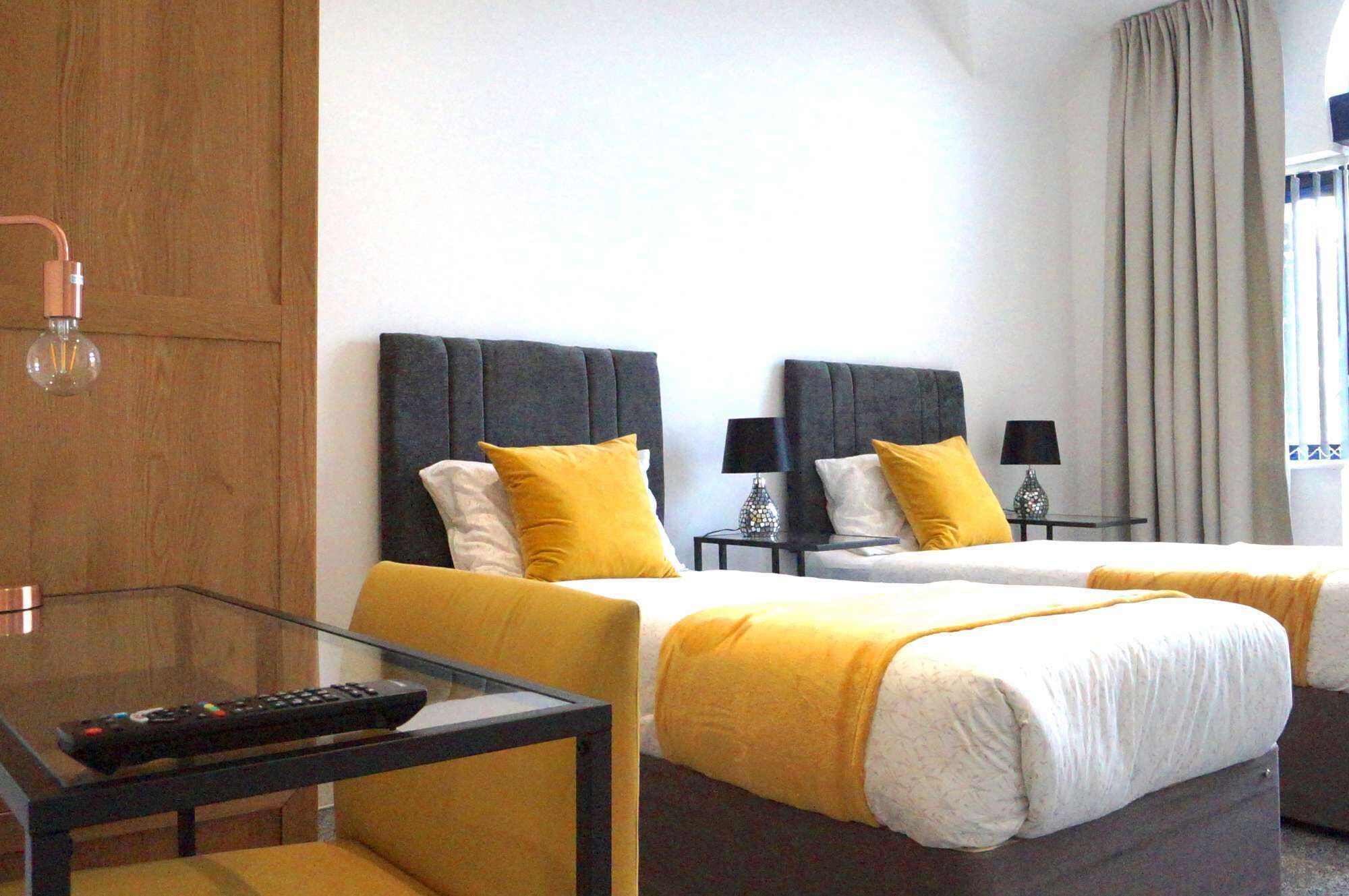 A hotel room with two beds, a glass table, and a remote control on the table.