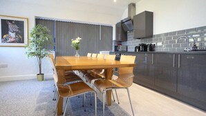 Una cocina moderna con armarios oscuros, un microondas y una cafetera. Hay una mesa de comedor con sillas y un florero con flores.