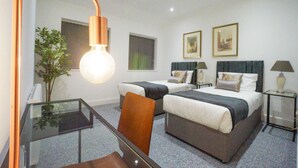 Habitación de hotel con dos camas, un escritorio de vidrio, una silla, un espejo grande y una lámpara del techo.