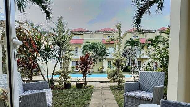 A patio area with wicker furniture, a pool, and a view of a building with red roofs. - Secure & Peaceful Residence – Beach 600m & Nearby Amenities (Flic-en-Flac)