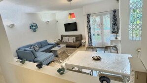 A living room with a sofa, a TV, a dining table, and a balcony with curtains. - Secure & Peaceful Residence – Beach 600m & Nearby Amenities (Flic-en-Flac)