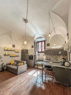 A spacious living area with a sofa, a dining table, and a kitchen with a stove and sink. - La dimora di GI - Nel centro storico di Viterbo (Viterbo)