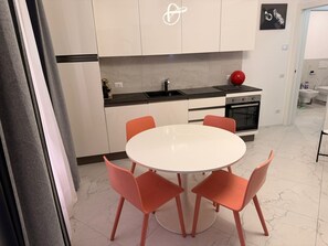A modern kitchen with a round table and orange chairs, a black countertop, and a red spherical object on the stove.