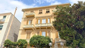 A multi-story building with balconies, a tree in the foreground, and a clear sky. - Henry House (Lavagna)