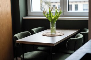 Ett matbord med en genomskinlig glasvas som innehåller vita blommor, omgivet av fyra stoppade stolar.