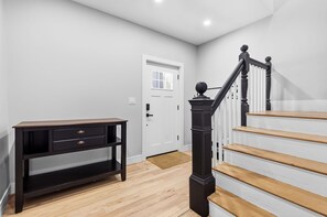 Un escalier avec des marches en bois et une balustrade noire, une porte blanche et une console en bois foncé dotée de tiroirs.