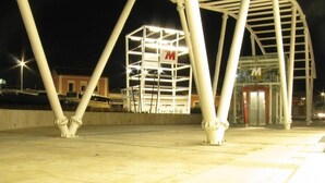 Vista noturna de um edifício com um grande letreiro 'M', entrada de vidro e estrutura em metal.