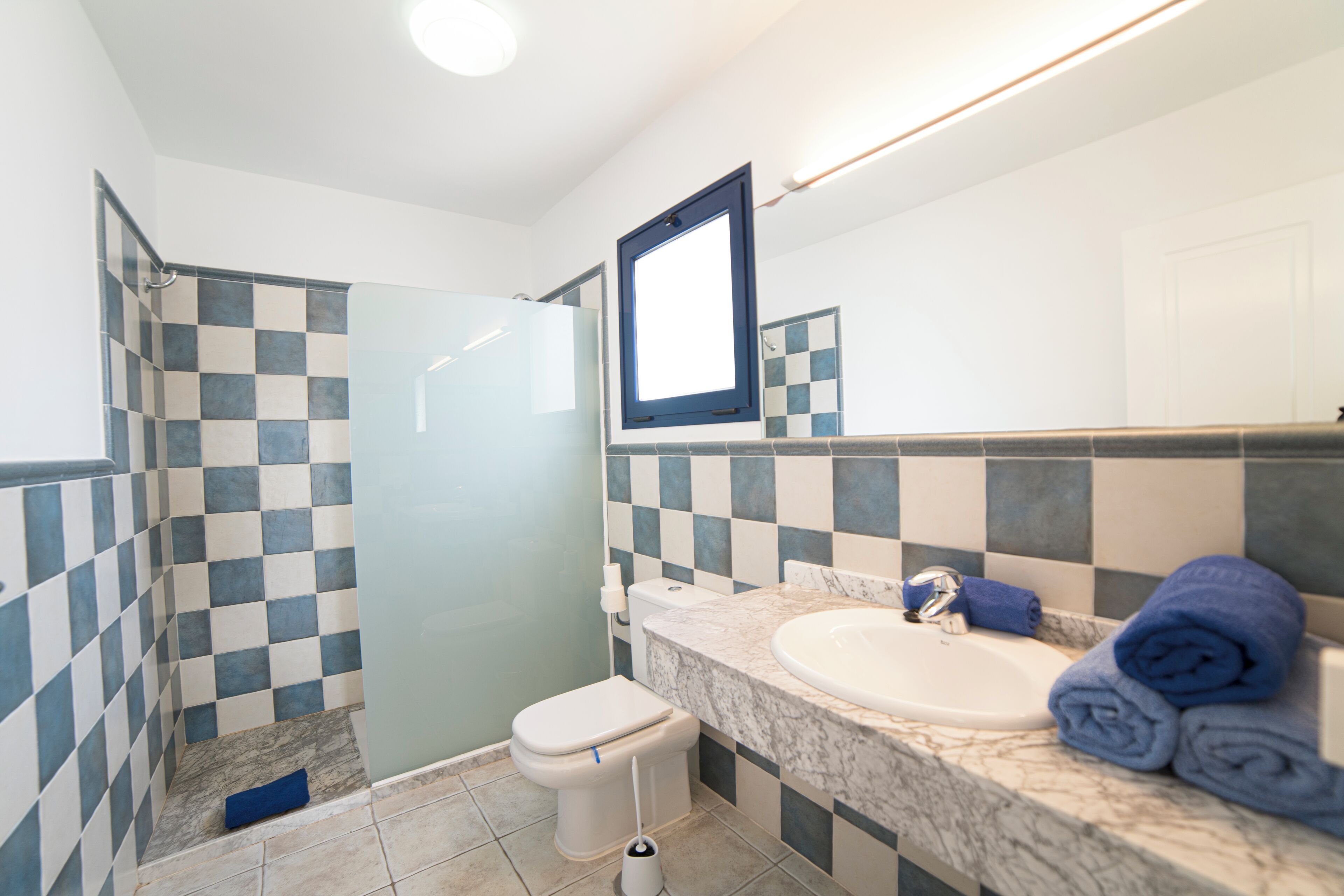 Une salle de bain avec un mur recouvert de carreaux à motifs géométriques, des toilettes, un lavabo doté d’un plan de travail en marbre et un miroir.