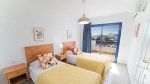 Una camera d'albergo con due letti, una testiera in legno, un comodino e una lampada a soffitto. Si vede una finestra con vista.