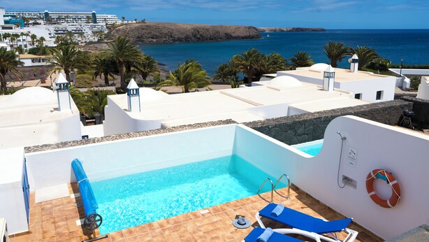Una piscina sul tetto con vista libera sul mare, palme e un edificio in lontananza.