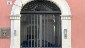 Entrada de um edifício com um grande portão de metal, uma placa e uma pequena placa acima do portão.