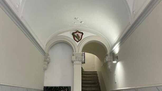 Uma escadaria imponente com paredes brancas e um emblema decorativo no topo.