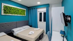 Quarto de hotel com duas camas, televisão, escrivaninha e janela com cortinas.