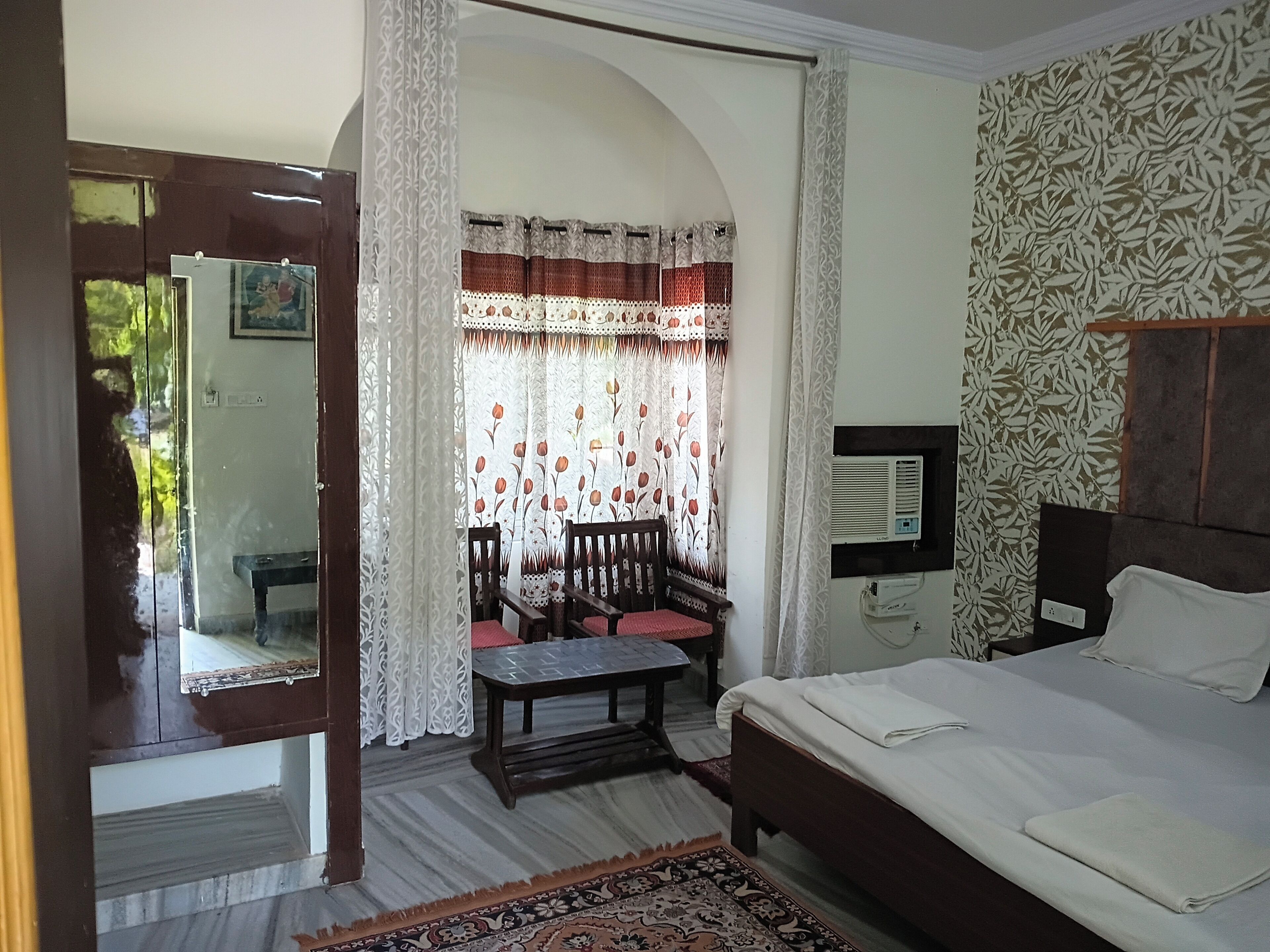 Une chambre à coucher avec un lit, un bureau, des chaises, un miroir et une fenêtre avec des rideaux.