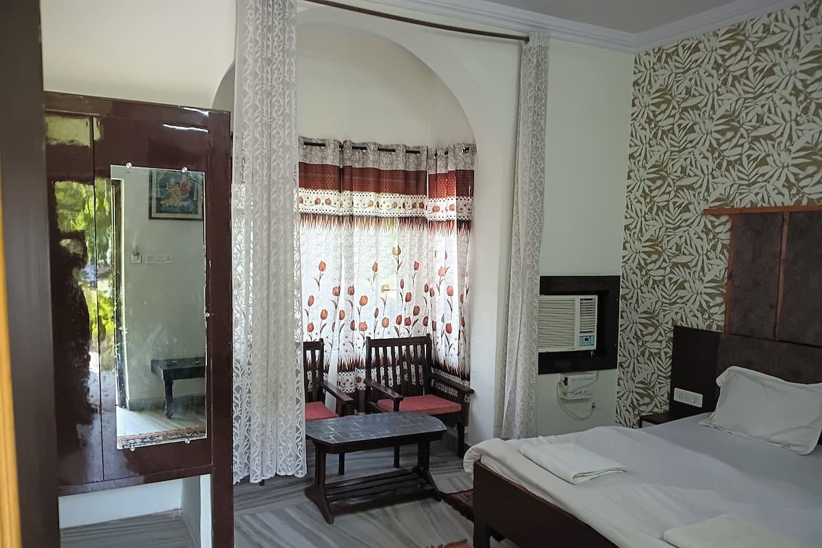 A bedroom with a bed, a desk, chairs, a mirror, and a window with curtains.