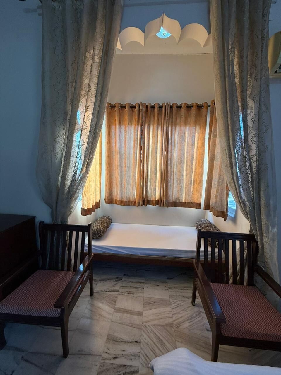 Une pièce avec un lit, deux chaises, un sol à motifs et des rideaux.