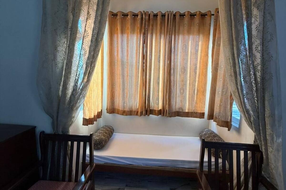 A room with a bed, two chairs, a patterned floor, and curtains.