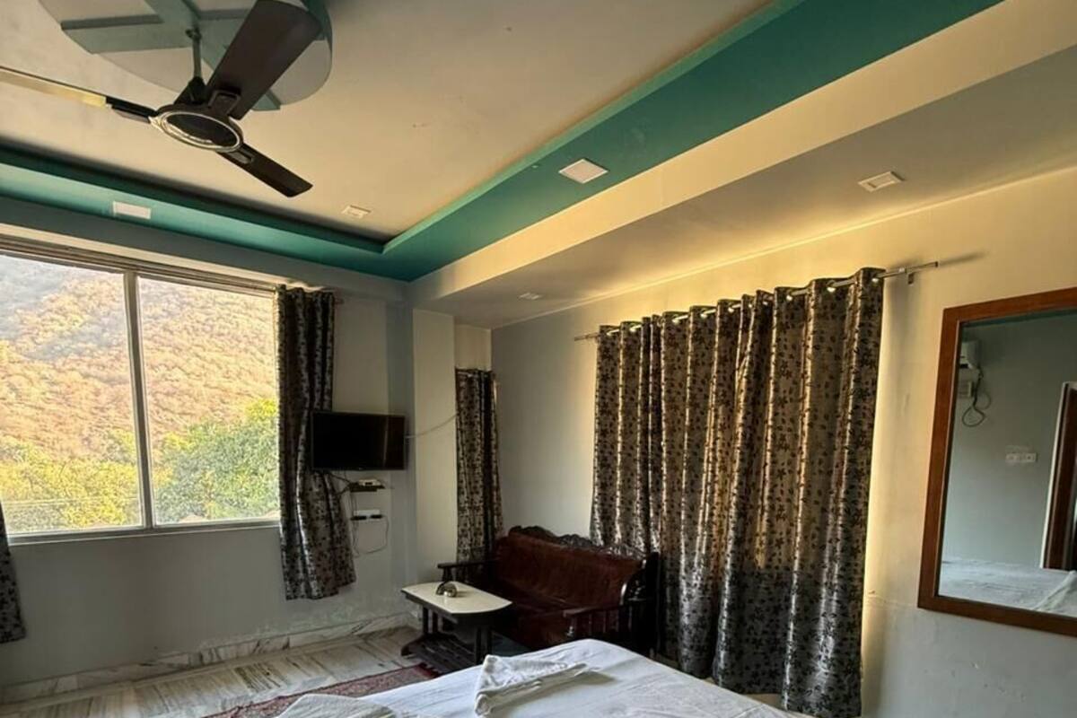 A hotel room with a bed, a desk, a chair, a ceiling fan, and a window with curtains.