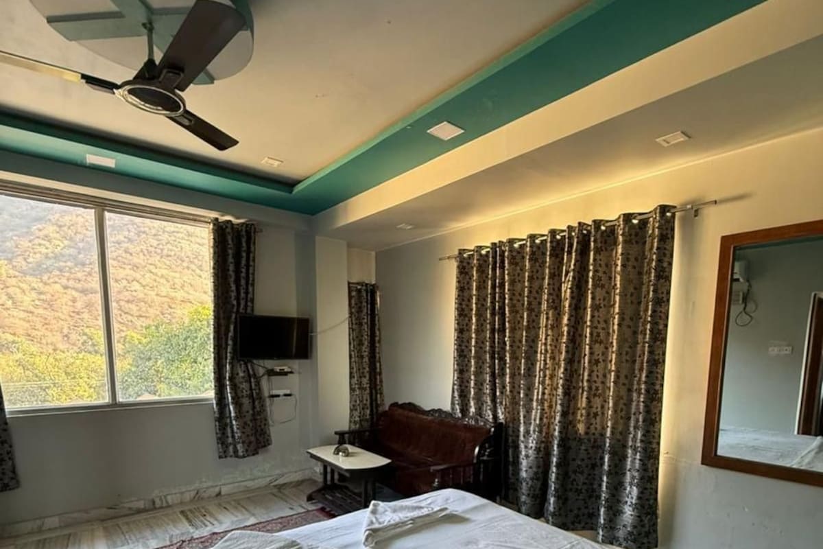 A hotel room with a bed, a desk, a chair, a ceiling fan, and a window with curtains.
