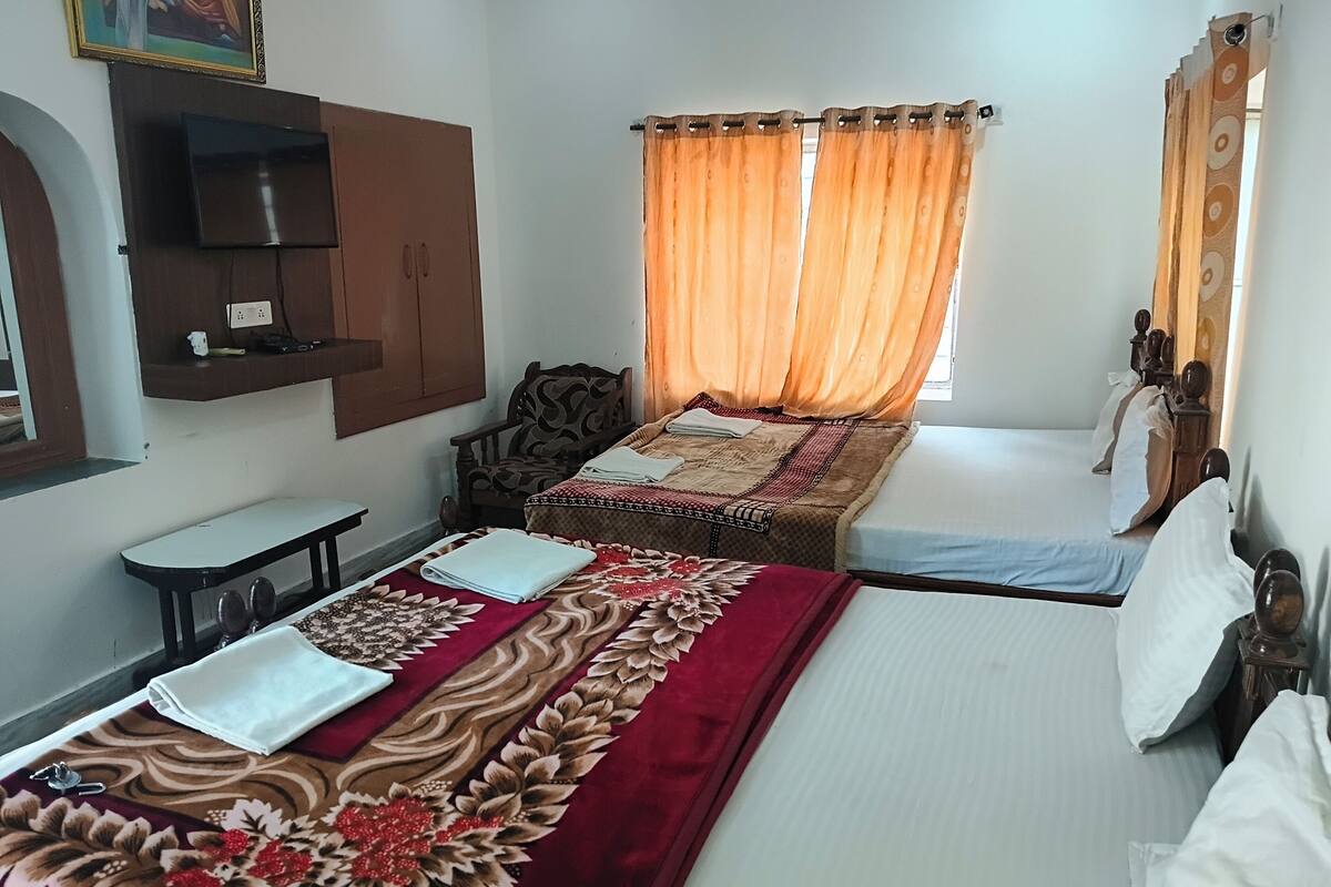 A hotel room with two beds, a TV mounted on the wall, a chair, and a small table.