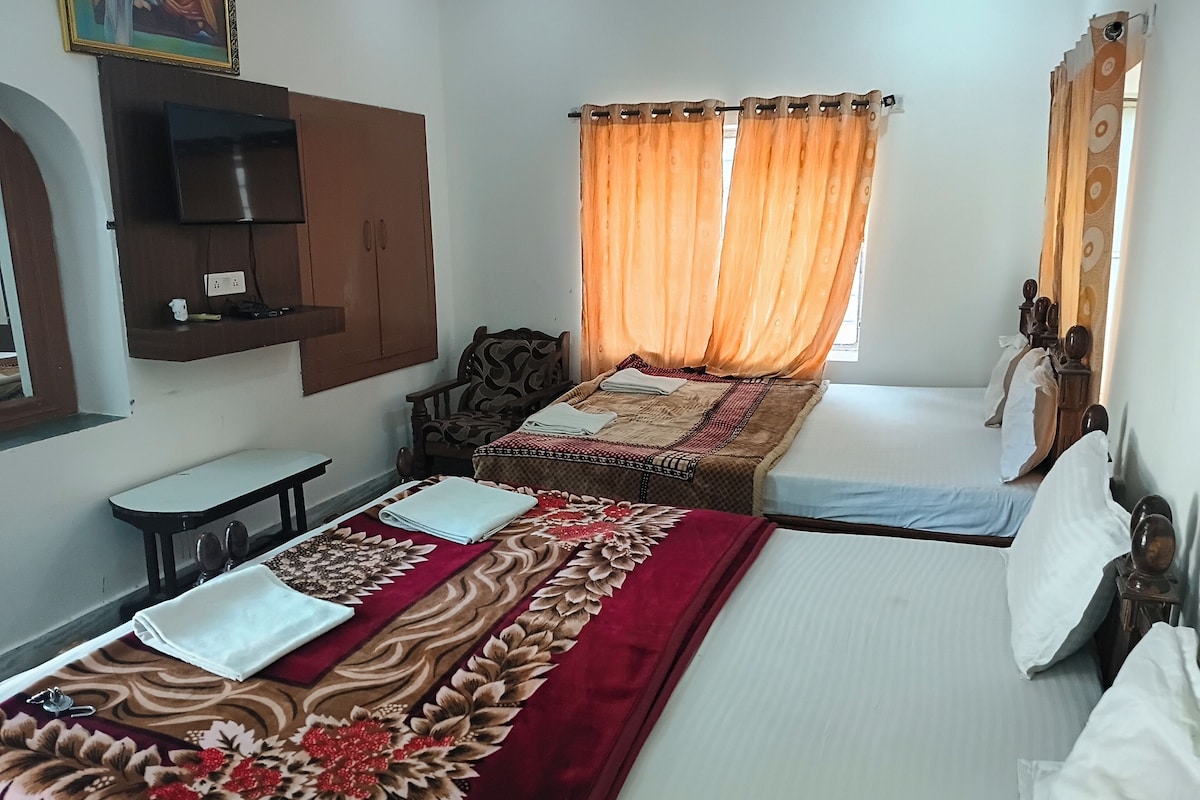 A hotel room with two beds, a TV mounted on the wall, a chair, and a small table.