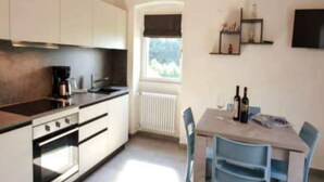 A kitchen with a window, a dining table with chairs, and a radiator. - Promotion - two-room apartment with private terrace Wormwood (Cadignano)
