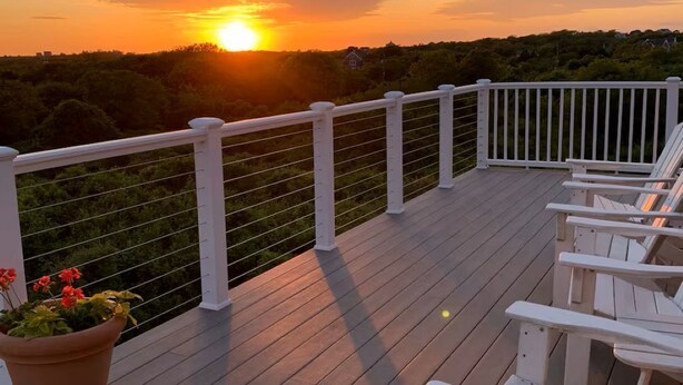 Une terrasse en bois avec des rampes blanches, un pot de fleurs et des chaises blanches.