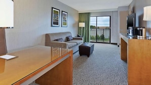 A hotel room with a sofa, a small table, a television, and a balcony with a view. - Embassy Suites By Hilton Auburn Hills (Auburn Hills)