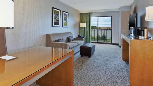 A hotel room with a sofa, a small table, a television, and a balcony with a view. - Embassy Suites By Hilton Auburn Hills (Auburn Hills)