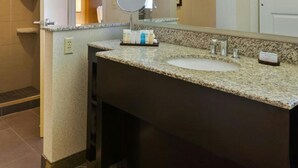 A bathroom with a granite countertop, a round mirror, and a white sink. - Embassy Suites By Hilton Auburn Hills (Auburn Hills)
