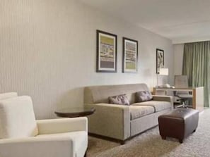 Una habitación de hotel con sofá, una silla, una mesita y una lámpara.