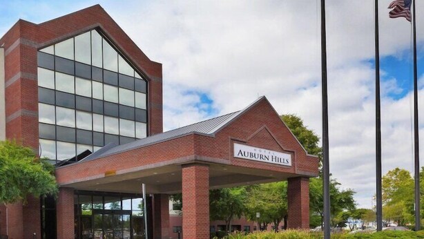 A hotel with a modern glass facade, a covered entrance, and a sign reading 'Auburn Hills.' - Embassy Suites By Hilton Auburn Hills (Auburn Hills)
