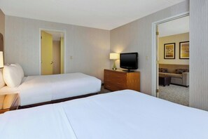 A hotel room with two beds, a television on a wooden dresser, and a door leading to a living area. - Embassy Suites By Hilton Auburn Hills (Auburn Hills)