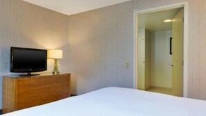 A hotel room with a bed, a TV on a wooden dresser, and a door leading to another room. - Embassy Suites By Hilton Auburn Hills (Auburn Hills)