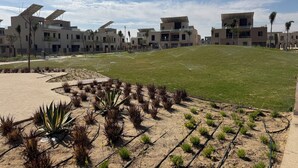 A modern residential area with flat-roofed buildings, a grassy hill, and a paved walkway.