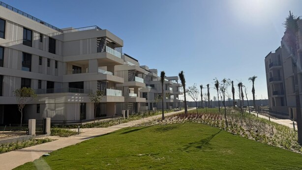 A modern multi-story building with balconies, a well-maintained lawn, and a clear sky.