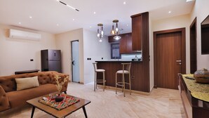 A modern living room with a sofa, a coffee table, and a kitchen area with a bar and stools.
